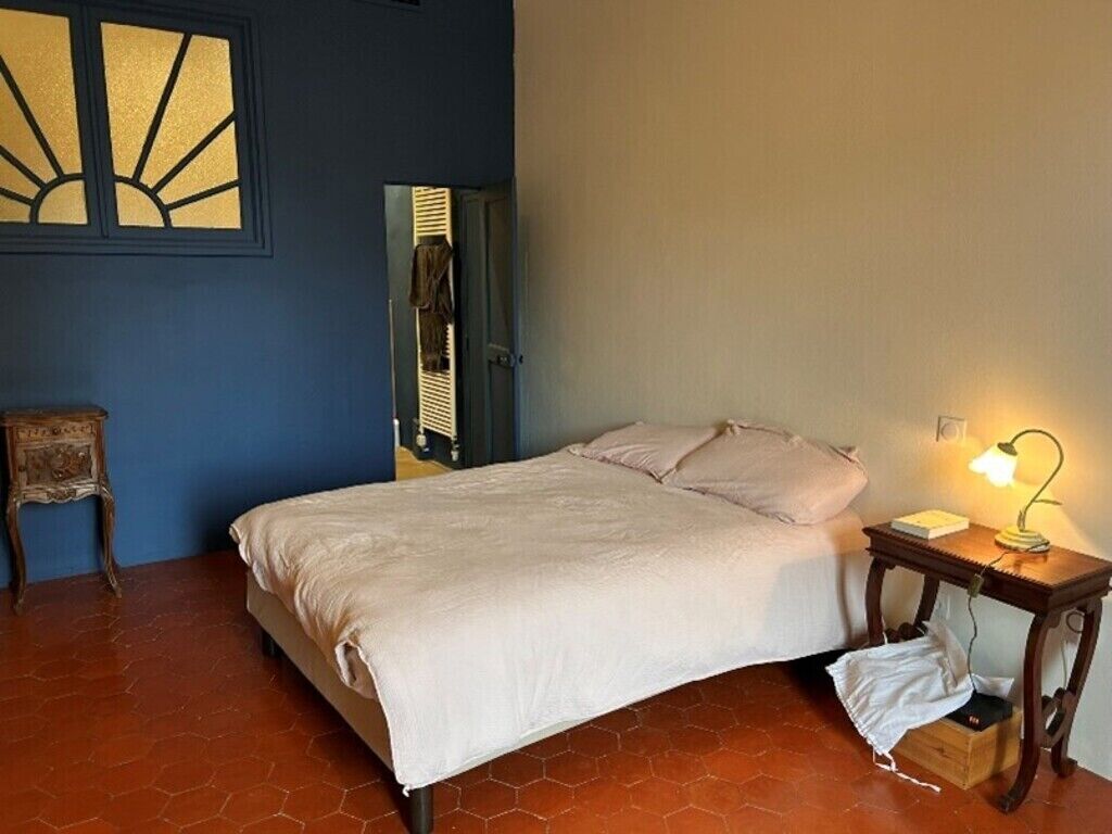 Un dormitorio con cama, mesita de noche con lámpara, una silla y un panel decorativo en la pared.