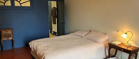 Un dormitorio con cama, mesita de noche con lámpara, una silla y un panel decorativo en la pared.
