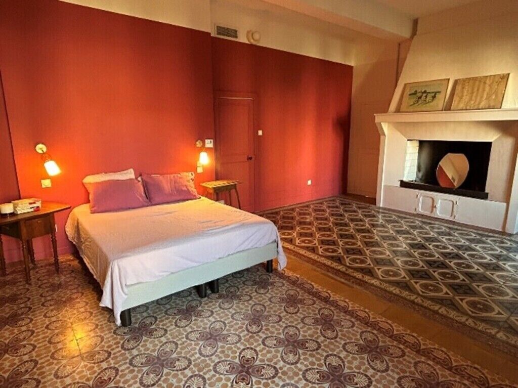 A bedroom with a bed, two bedside tables, a patterned rug, a fireplace, and a red accent wall.