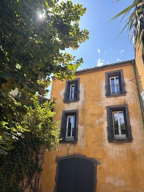 A building with three windows and a large door, surrounded by greenery.