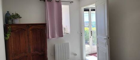Ett sovrum med en trägarderob, ett element, ett fönster med gardin och utsikt över omgivningen.