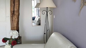 Una stanza con un divano in pelle bianca, un trave in legno, uno specchio, una lampada da terra e un elemento decorativo a parete.