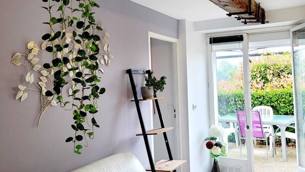 Un soggiorno con un divano bianco, piante sospese, una scala e vista sul giardino tramite porte in vetro.
