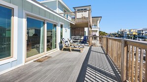 A modern house with a wooden deck, large sliding glass doors, and a balcony with lounge chairs.