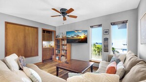 A living room with a wooden coffee table, beige sofas, a bookshelf, and a ceiling fan.
