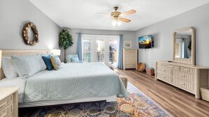 A bedroom with a bed, dresser, TV, and ceiling fan.