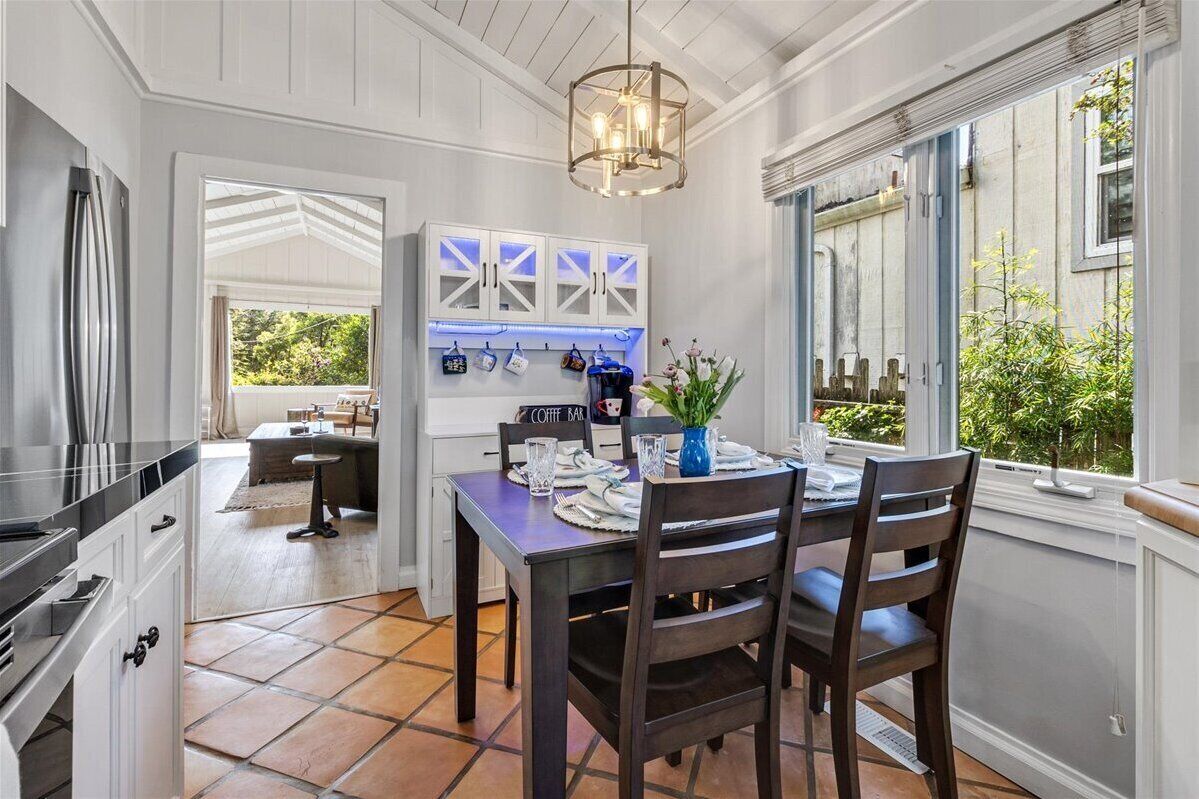 A dining area with a table set for two, a hanging light fixture, and a view of the outdoors.