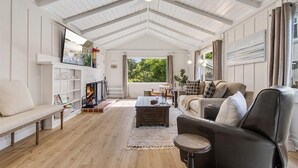 Un vaste salon doté d’un haut plafond, d’un plancher en bois, d’une cheminée, d’un ensemble de canapés et d’une grande fenêtre offrant une vue sur la verdure.