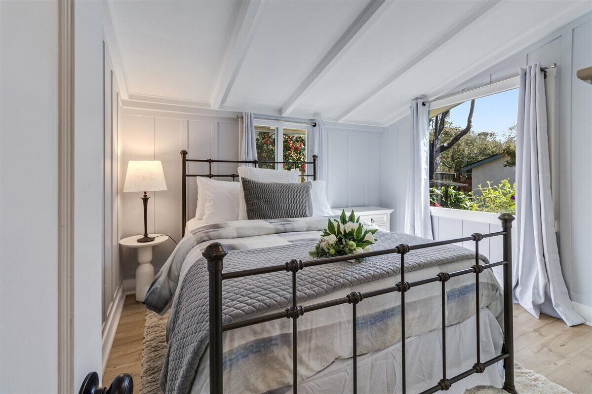 A bedroom with a bed, bedside table, lamp, and a window with curtains.