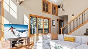 Ein geräumiges Wohnzimmer mit einem großen Flachbildfernseher, einem weißen Sofa und einer Holztreppe.