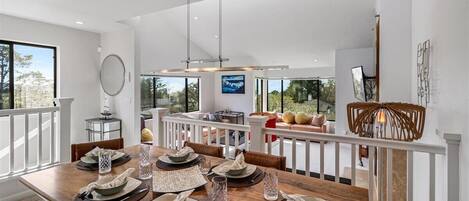 A dining area with a wooden table set for six, white railings, and a view of the outdoors.