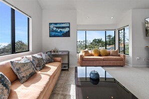 A modern living room with a beige sofa, a glass coffee table, and a view of the outdoors.