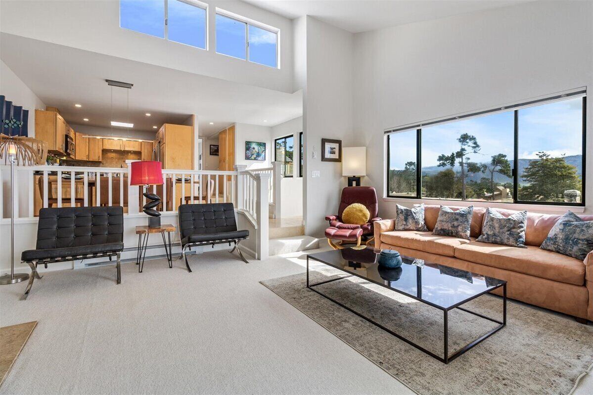 A spacious living area with a sofa, two black chairs, a glass coffee table, and a view of the outdoors.