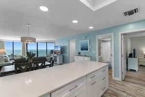 A modern kitchen with a large island, a dining area with a view, and a bathroom with a shower and toilet. - Condo with Ocean Views & Private Balcony, Near Pier (Garden City Beach)