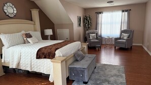 A bedroom with a large bed, a bench, two chairs, a small table, and a window with curtains. - Modern Southern Charm Near Airport & Downtown ATL (Riverdale)