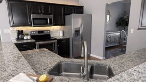A kitchen with granite countertops, stainless steel appliances, and dark cabinetry. - Modern Southern Charm Near Airport & Downtown ATL (Riverdale)