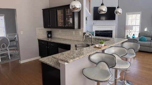 A modern kitchen with granite countertops, black cabinets, and a central island with bar stools. - Modern Southern Charm Near Airport & Downtown ATL (Riverdale)