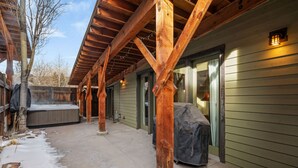 A covered outdoor area with wooden beams, a hot tub, and a covered grill. - Town Center Retreat | Hot Tub | Grill | 10 min to resort (Big Sky)