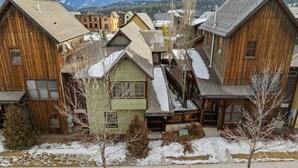 A cluster of wooden buildings with a snowy landscape and mountains in the background. - Town Center Retreat | Hot Tub | Grill | 10 min to resort (Big Sky)