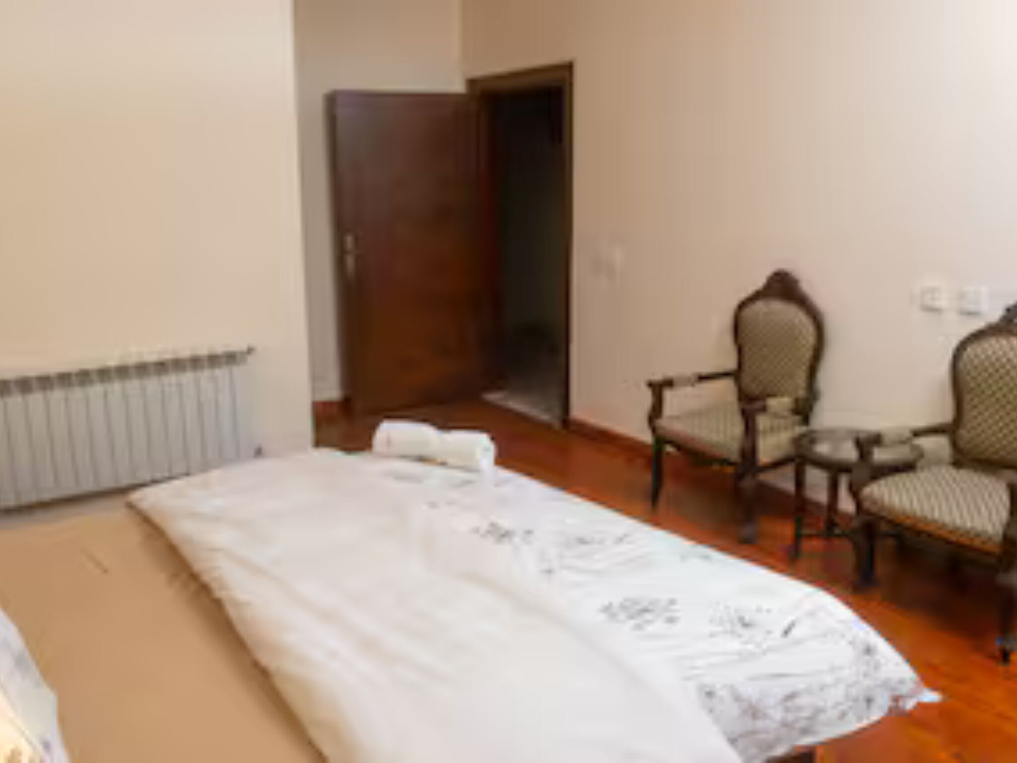 Un dormitorio con una cama, una silla, una mesita y una puerta que da a otra habitación.