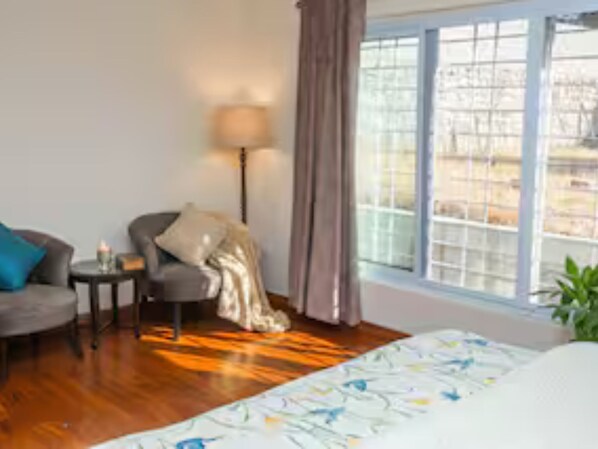 Une chambre d’hôtel avec un lit, un canapé, une chaise, une petite table avec une lampe et une fenêtre avec des rideaux.