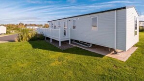 Une maison mobile de plain-pied dotée d’une terrasse clôturée, d’un petit porche et d’une allée pavée.