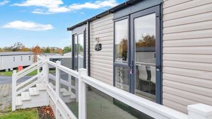 Une maison mobile à l’extérieur blanc, dotée de grandes fenêtres et d’une balustrade de véranda blanche.