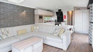 Un salon moderne avec un canapé d’angle, une table basse et un coin cuisine à l’arrière-plan.