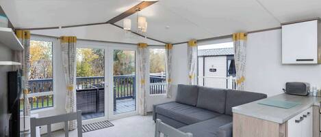 A modern, well-lit room with a grey sofa, a dining table, and a kitchen area.