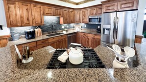 Una cocina con armarios de madera, encimeras de granito, un refrigerador de acero inoxidable, un microondas, una estufa y una cafetera.