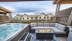 Un jacuzzi, una fogata y un sofá en una terraza con vistas a casas al fondo.