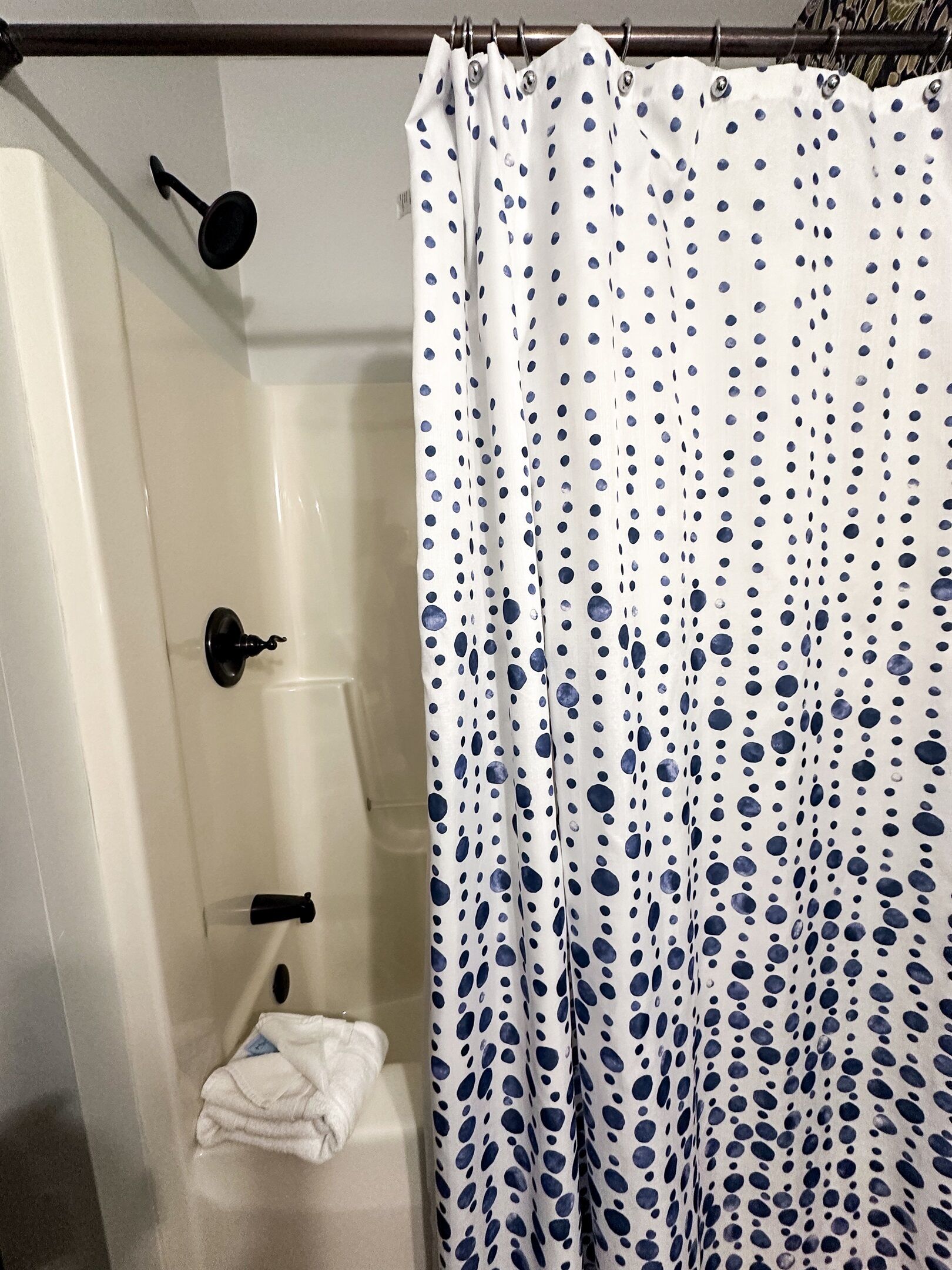 A shower area with a white shower curtain featuring blue polka dots.