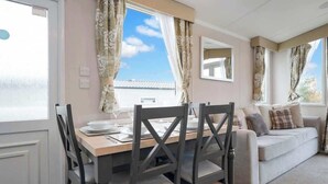 A dining area with a table set for four, a sofa, and a window with curtains. - Seton Sands Gullane Luxe Lodge 3BR Sleeps 8 | WiFi (Port Seton)