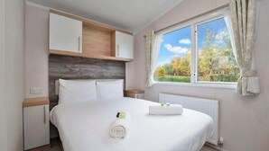 A bedroom with a bed, a nightstand, a wardrobe, and a window with a view of trees. - Seton Sands Gullane Luxe Lodge 3BR Sleeps 8 | WiFi (Port Seton)