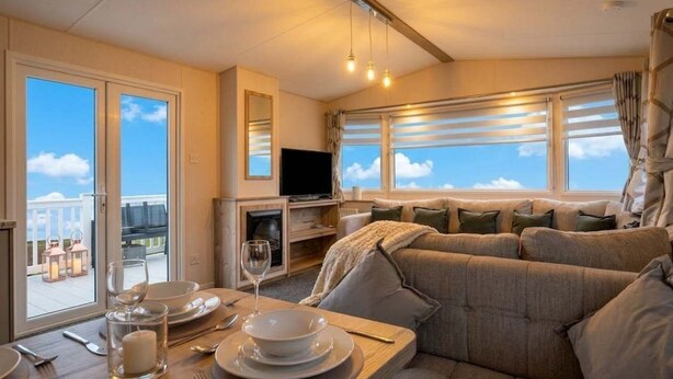 A cozy living area with a sofa, dining table set for two, a flat-screen TV, and large windows offering a view of the sky.