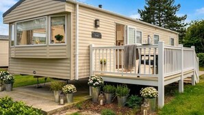 A mobile home with a deck, potted plants, and a sign that reads 'Treff.'