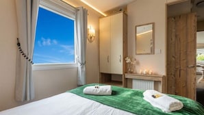 A hotel room with a bed, a window with curtains, a wardrobe, a mirror, and a small table with candles.