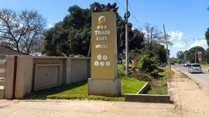 Μια πινακίδα για το ξενοδοχείο Train Luxe, με καθαρή θέα στην γύρω περιοχή, η οποία περιλαμβάνει έναν δρόμο, πράσινο και ένα κτίριο στο βάθος.