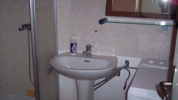 Un baño con un lavamanos blanco, cabina de ducha con vidrio y un inodoro blanco.