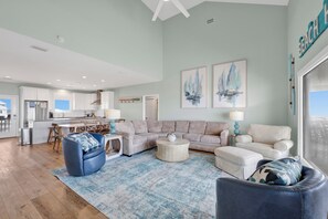 A spacious living area with a large sofa, a coffee table, and a blue armchair. There is a kitchen in the background with modern appliances. - Beachfront | Pet Friendly | Private Boardwalk | Game Room (Gulf Shores)