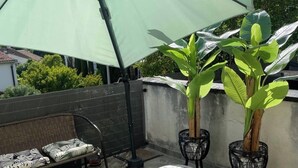 A patio area with a large umbrella, two potted plants, a wicker sofa, and a round ottoman. - Large family home near the canal in Agen (Agen)