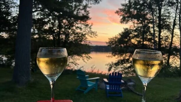 Two glasses of white wine on a table with a view of a lake and chairs in the background. - Sunsets on Beaver Dam Lake (Cumberland)