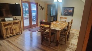 A dining area with a wooden table and chairs, a television on a cabinet, and a door leading outside. - Sunsets on Beaver Dam Lake (Cumberland)