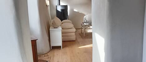 Un couloir étroit au plancher en bois, avec un canapé blanc et une petite table sur laquelle se trouve un panier.