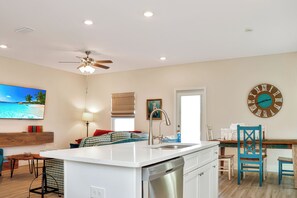 A modern kitchen with a built-in dishwasher, a dining area with a wooden table and chairs, and a large wall clock.
