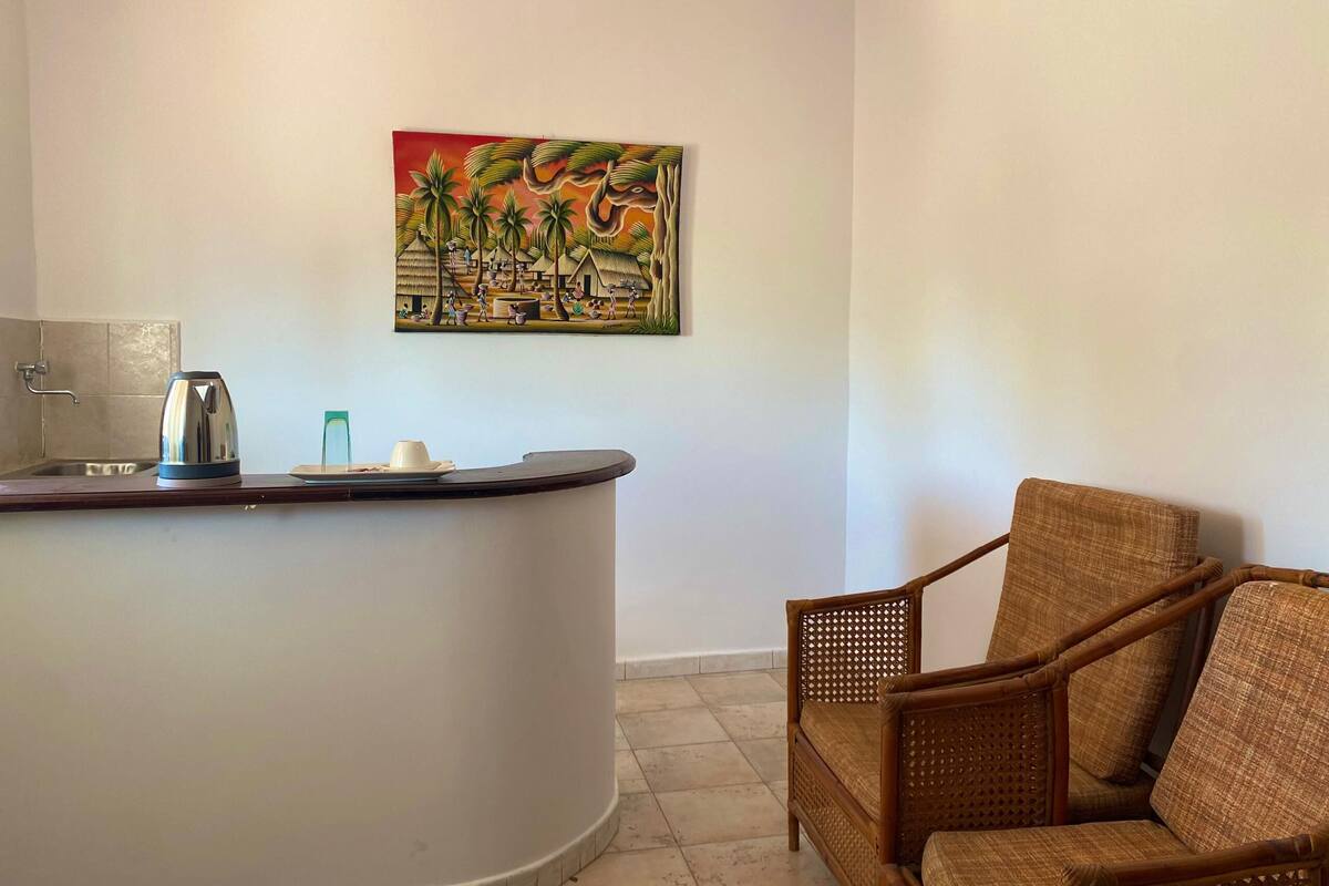A room with a kitchen counter, a kettle, a plate, and a chair.