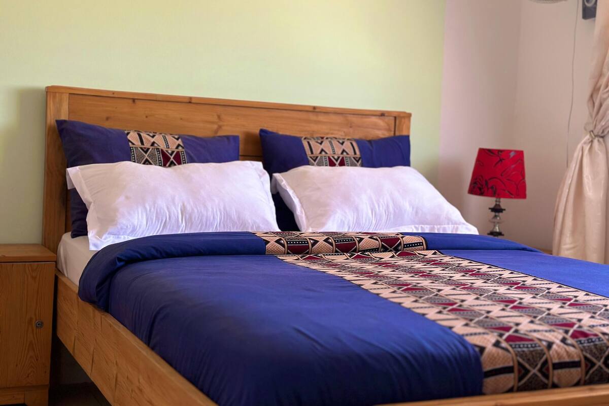 A bed with a wooden headboard, two white pillows, and a blue bedspread with a patterned blanket.