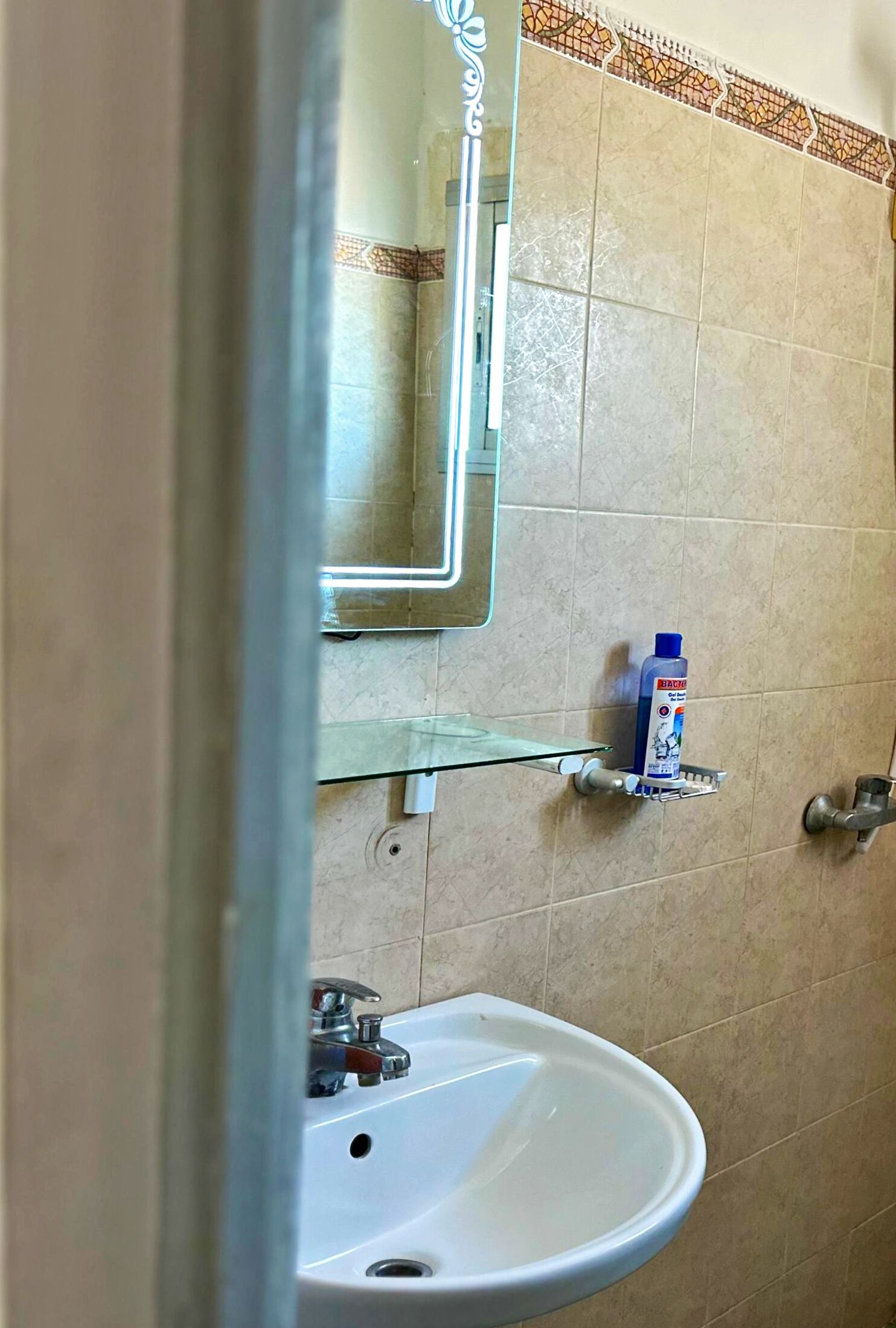 A bathroom with a sink, mirror, and a shelf with a bottle.