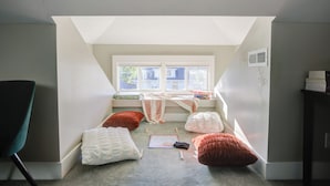 A small attic bedroom with a sloped ceiling, a window, and a view of the outside. There are pillows and a game on the floor. - Cozy Fountain Square Retreat Just Steps from Downtown Indianapolis (Indianapolis)