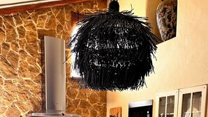 Eine rustikale Küche mit einer Steinwand, einer schwarzen Hängeleuchter und einem Essbereich mit einem gestreiften Tischläufer und schwarzen Stühlen.